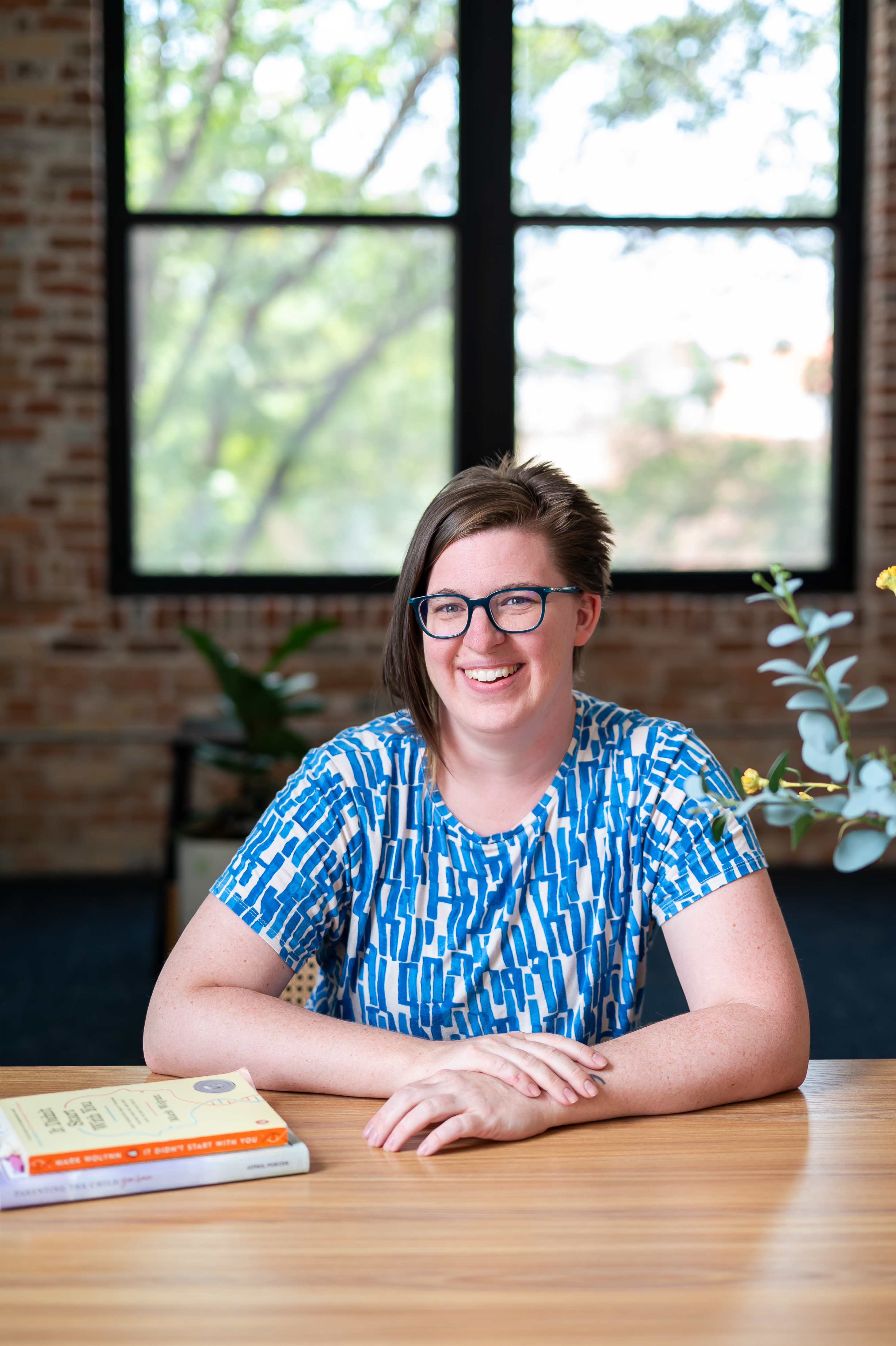 Heidi Lindemann, Colorado therapist, smiling and relaxed at her desk with therapy and mindfulness books nearby